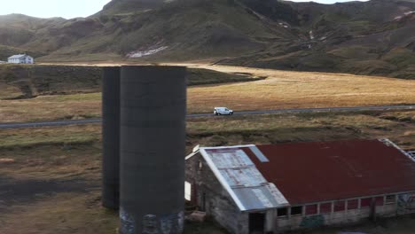 Rural-Iceland-valley-with-abandoned-farm-building,-car-traveling-on-remote-road,-aerial