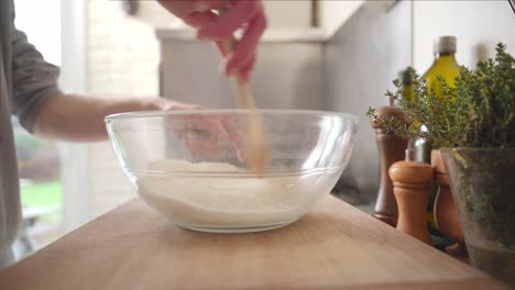 Person-finishing-mixing-ingredients-in-a-bowl-with-a-wooden-spoon-on-top-of-a-wooden-cutting-board-then-putting-the-bowl-away