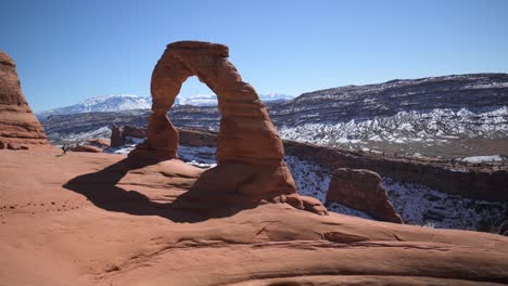 Hiker-walking-up-to-and-climbing-on-the-Delicate-Arch-in-Arches-National-Park,-pan