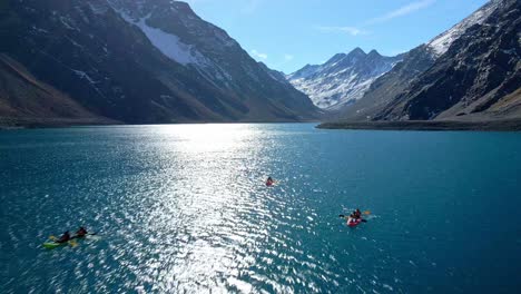 Aerial-view-dolly-in-of-three-kayaks-in-the-Laguna-del-Inca-with-the-sun-reflecting-on-the-crystal-blue-water,-snowcapped-mountains-in-the-background