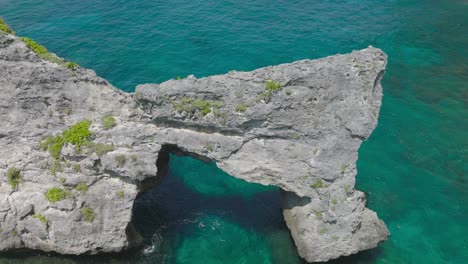 Rock-arch-cliff-surrounded-by-shallow-blue-turquoise-water,-aerial