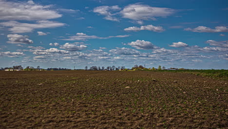 Timelapse-shot-of-white-clouds-along-beautiful-sky-over-ploughed-spring-field-beside-a-highway-at-daytime
