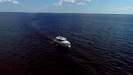Aerial-drone-shot-of-modern-white-motor-boat-along-the-horizon-on-dark-water,-drone-at-daytime