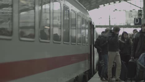 Passengers-get-off-train-onto-platform-with-their-luggage,-train-departs