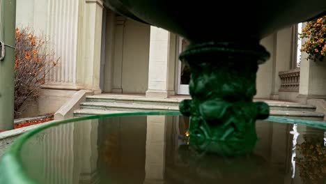 Handheld-pan-right-of-the-Bruna-Palace-with-its-reflection-in-the-ornamented-fountain-outside,-heritage-day-in-Santiago,-Chile