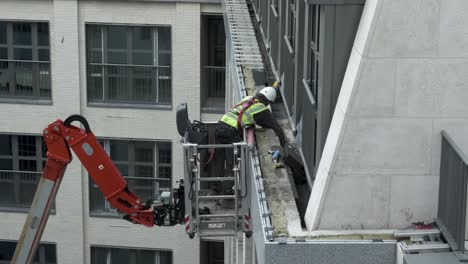 Construction-Worker-In-Cherry-Picker-Fixing-Tiles-To-Outside-Of-New-Apartment-Build-In-Central-London