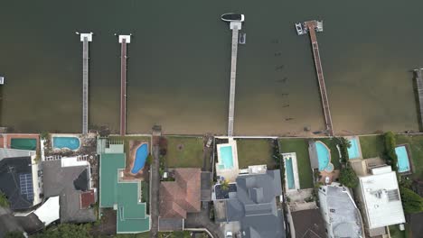 Aerial-top-down-flyover-the-rooftops-of-waterfront-properties-with-boat-decks-beside-the-ocean
