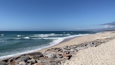 waves-washing-on-long-sand-beach-with-rocks,-Furadouro,-Portugal