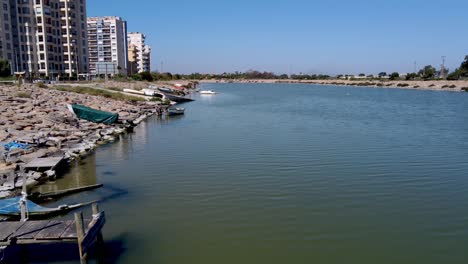 The-Segura-River-flows-to-the-ocean-on-the-coast-of-Spain-with-old-and-sunken-boats-along-the-shore-by-apartment-buildings