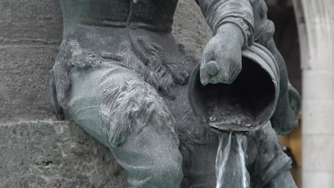 Nahaufnahme-Von-Wasser,-Das-Von-Einer-Der-Bronzestatuen-Am-Fischbrunnen-Auf-Dem-Marienplatz-Im-Herzen-Münchens-Aus-Einem-Korb-Gegossen-Wird
