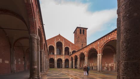 Time-lapse-of-Saint-Ambrogio-church-brick-building-with-bell-towers,-courtyard,-arches-at-overcast-day,-Milan,-Lombardy,-Italy