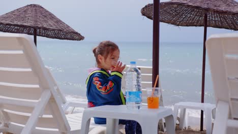 Kaukasisches-Kleines-Mädchen,-Das-Ein-Glas-Orangensaft-In-Zeitlupe-Am-Strand-Trinkt