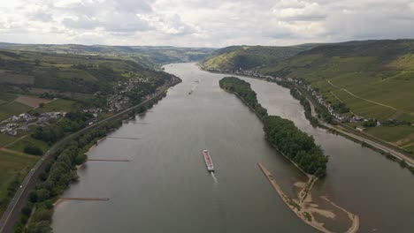Long-cargo-ship-traveling-along-the-rhine-river-between-lush-meadows-and-vineyards-on-a-sunny-day
