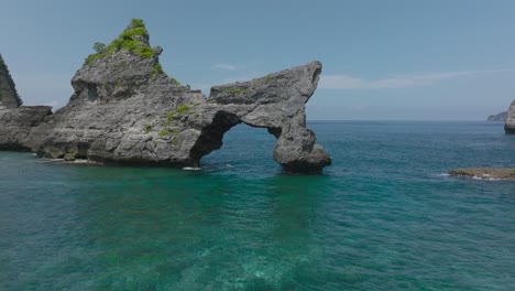 Natural-rock-arch-cliff-formation-near-shore-of-Atuh-Beach,-Nusa-Penida,-aerial