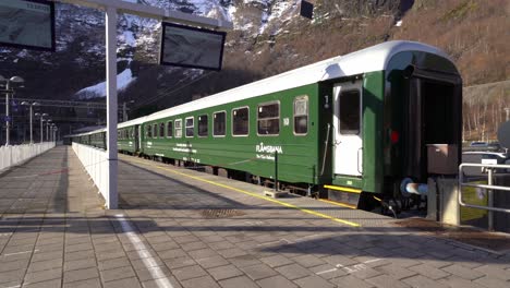 Flamsbanen-station-in-Flam-Norway---Walking-towards-green-train-waiting-on-platform-during-sunny-spring-day