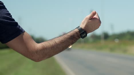 Man-points-thumb-to-hitchhike-on-roadside,-close-up