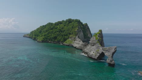 Nusa-Batupadasan-island-with-famous-rock-arch-formation,-aerial-view