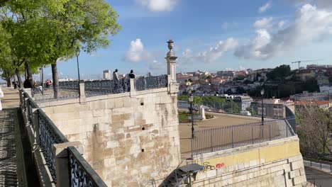 People-walking-at-Miradouro-de-São-Pedro-de-Alcântara,-viewpoint-with-amazing-Lisbon-cityscape-view