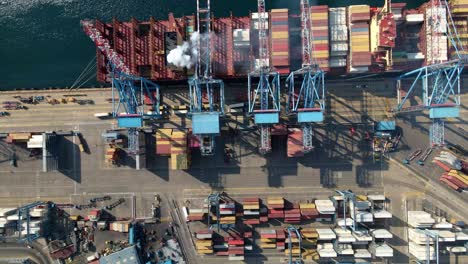 Aerial-top-down-truck-right-of-cranes-loading-containers-on-a-cargo-ship-docked-in-Valparaiso-Sea-Port,-Chile
