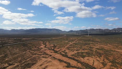 Drone-aerial-moving-towards-a-wind-farm-in-country-Australia-with-mountains-in-the-background-and-a-bird-flying-nearby-on-summer-day