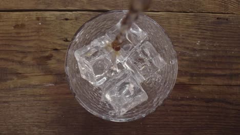Pouring-beer-into-a-transparent-glass-with-ice-cubes-laying-at-the-bottom