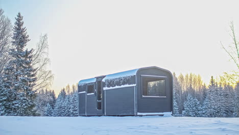 Timelapse-shot-of-rectangular-wooden-cabin-surrounded-by-thick-layer-of-snow-during-winter-season-on-a-cloudy-day-with-trees-in-the-background