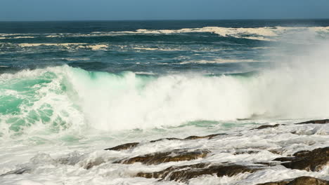 Wave-collides-dramatically-on-rocky-shore,-big-splash