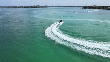 Camera-moves-in-a-circle-around-a-speed-boat-pulling-a-towable-in-an-ocean-near-a-beach