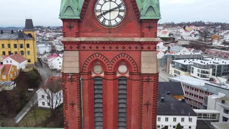Trinity-church-Arendal-Norway-closeup-of-tower---Aerial-slowly-moving-upwards-along-church-tower-to-reveal-clock-and-city-background