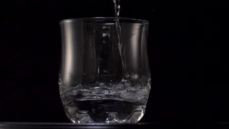 Agua-Limpia-Cayendo-En-Un-Vaso-Transparente,-Sobre-Un-Fondo-Negro