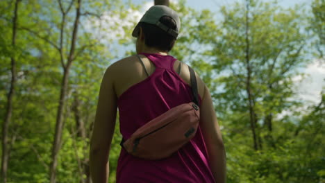 Siguiendo-A-Una-Mujer-Caminando-Por-El-Bosque-Con-Una-Pequeña-Riñonera-Alrededor-De-La-Espalda-Y-Vistiendo-Una-Camiseta-Sin-Mangas-Rosa