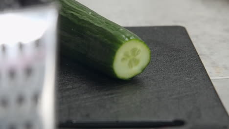 Close-up-dolly:-Cucumber-tip-cut-off-on-black-kitchen-cutting-board