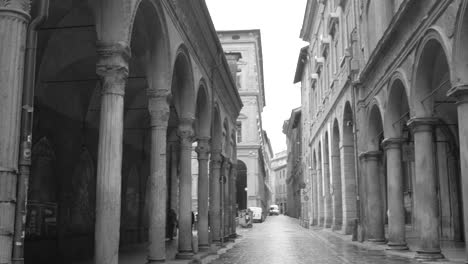 Black-and-white-shot-of-people-walking-by-the-sidewalk-under-Porticoes-at-Bologna-in-Northern-Italy-at-daytime