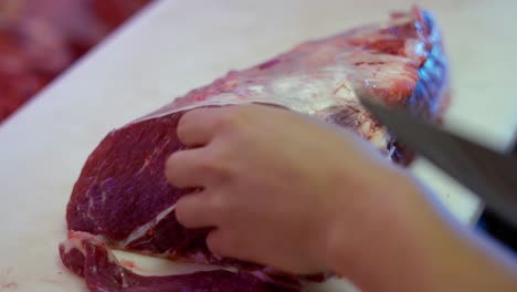 close-up-of-a-butcher´s-hands-with-a-knife-slicing-red-meat-over-a-white-board