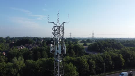 5G-broadcasting-tower-antenna-in-British-countryside-woodland-with-vehicles-travelling-on-highway-background-rising-aerial-view