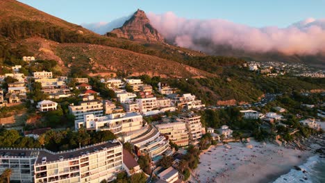sunset-of-hotels-at-Clifton-Beach-with-clouds-rolling-over-lions-head-in-Cape-Town,-aerial