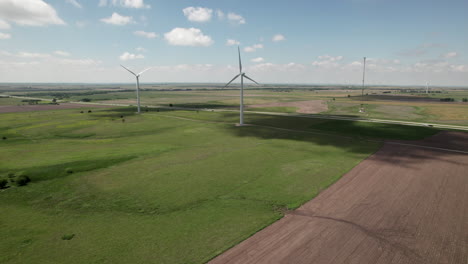 Turbines-rotate-slowly-in-wind-as-traffic-travels-on-state-highway-Aerial-turn