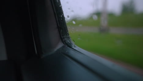 Wassertropfen-Plätschern-Und-Schimmern-In-Der-Ecke-Eines-Autofensters,-Während-Das-Auto-Fährt