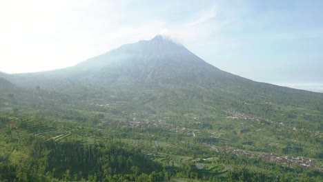 Langsamer-Vorwärtsflug-Aus-Der-Luft-über-Eine-Ländliche-Plantage-Mit-Dem-Vulkan-Merapi-Im-Hintergrund