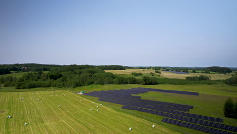 Aerial-landscape-of-a-small-solar-panels-farm-and-hay-bales-in-plastic-wraps-on-a-field-after-harvesting-crops
