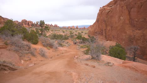 People-hiking-through-Arches-National-Park-towards-Landscape-Arch-on-a-cloudy-day,-tilt
