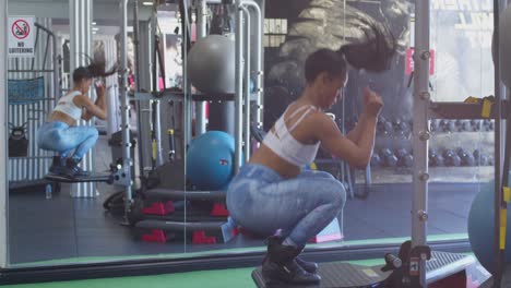 Sexy-Latina-Bodybuilder-Springt-Kniebeugen-Im-Fitnessstudio-Mit-Einem-Spiegel-Im-Hintergrund