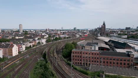 A-soaring-camera-flight-revealing-the-cathedral-and-main-train-station-with-the-empty-track-apron-of-Cologne,-Germany-on-a-summer-day