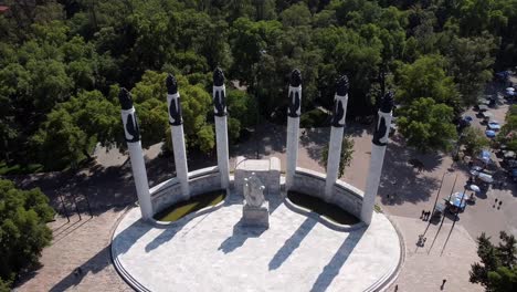 Aerial-drone-backwards-moving-shot-over-the-monument-of-the-children-heroes-in-the-Bosque-de-Chapultepec,-in-Mexico-City,-with-a-view-of-lush-green-vegetation-in-the-background