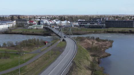 Flying-towards-small-town-Selfoss-in-Iceland-with-Ölfusárbrú-bridge-crossing-Olfusa-river,-aerial