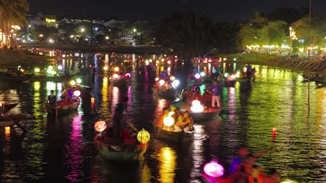 Timelapse-Night-View-of-Colorful-Hoi-An-Lantern-Festival,-Lantern-Lit-Nights,-Boats-Canoes-Traffic-Floating-Sailing-on-the-Canal-River,-Tourists-and-Glowing-Paper-Lanterns-on-Board