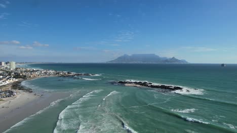ocean-waves-and-Table-Mountain-at-Big-Bay-Beach-in-Cape-Town,-aerial