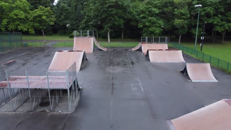 Aerial-view-flying-reverse-above-fenced-skate-park-ramp-in-empty-closed-public-playground