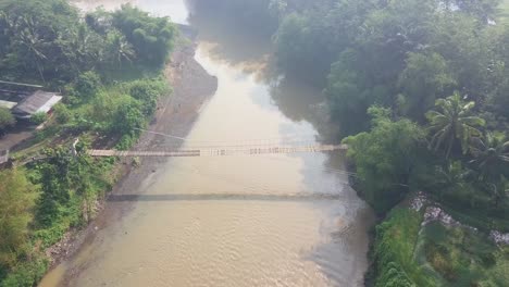 Poi-drohnenaufnahme-Der-Hängebrücke-über-Den-Fluss-Mit-Motorradüberquerung-Darauf-Morgens-Mit-Sonnenstrahl,-Zentral-java,-Indonesien