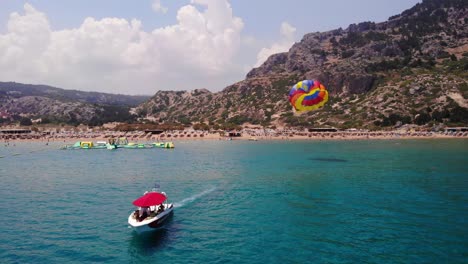 Parasailing---Speedboat-Towing-Tourists-Attached-On-Colorful-Parachute-In-Tsambika-Beach,-Rhodos,-Greece